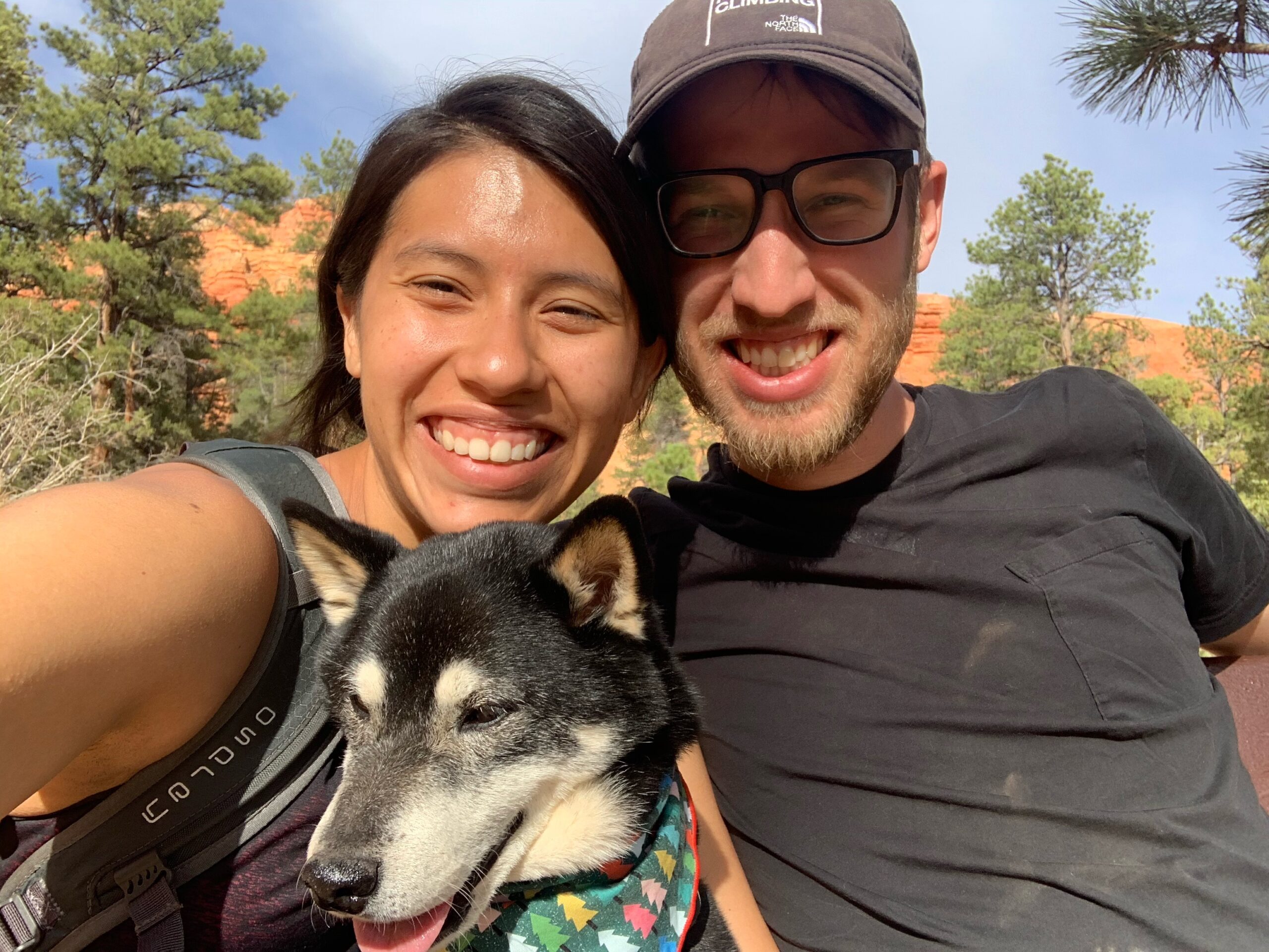 Dalia, Scott, and Beta smiling together outdoors in front of red rock cliffs.