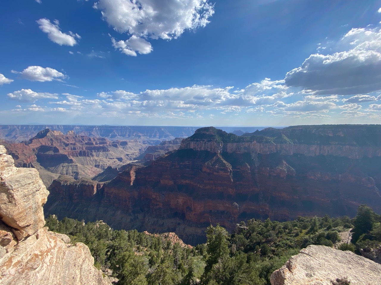 Layered cliffs and forested plateaus beneath a blue, cloud-filled sky at the Grand Canyon’s North Rim.